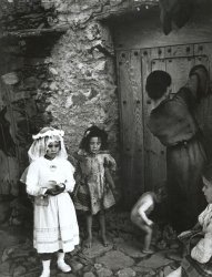 W. Eugene Smith - Lorenza Curiel in White First  Communion Dress Waiting for Her Mother to Lock Door (from 'Spanish Village')
